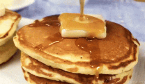 a stack of pancakes with butter and syrup being poured on top .