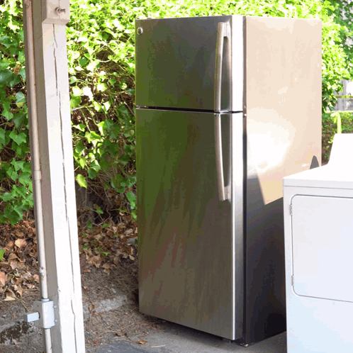 A Stainless Steel Refrigerator Is Sitting Next To A White Washer And Dryer GIF