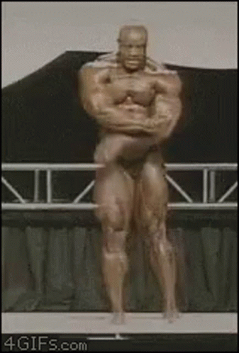 A Statue Of A Bodybuilder Is Standing On A Stage With His Arms Crossed GIF