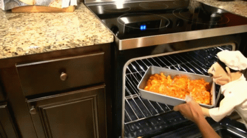 A Statue Of A Chef Is Holding A Pan Of Food In An Oven GIF