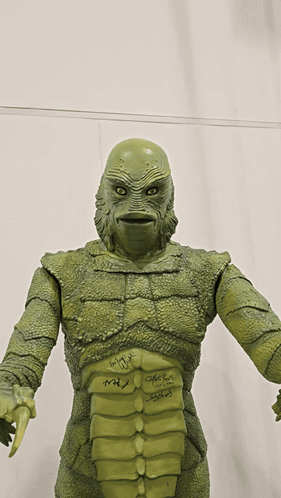 A Statue Of A Creature Has Signatures On It Including Those Of John Carpenter And Peter Fonda GIF