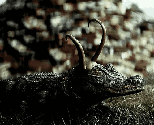 A Statue Of A Crocodile With Horns Laying In The Grass GIF
