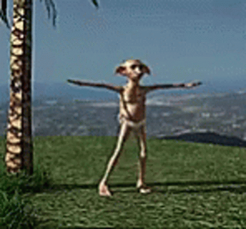 A Statue Of A Frog Is Standing In The Grass With His Arms Outstretched In Front Of A Palm Tree . GIF