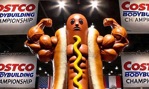 a statue of a hot dog with muscles and mustard is in front of costco banners