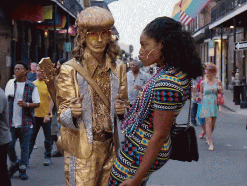 A Statue Of A Man Holding A Guitar Is Standing Next To A Woman Wearing Beads GIF