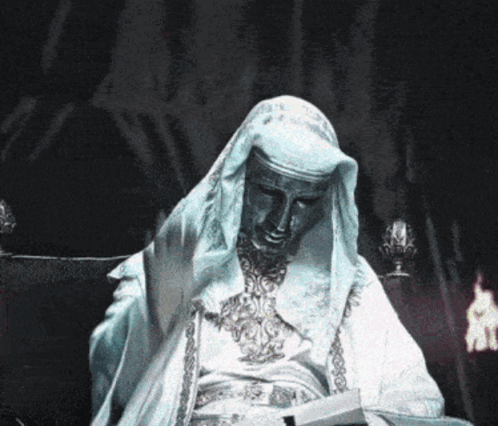 Statue Of Man In White Robe Sitting In Dark Room GIF