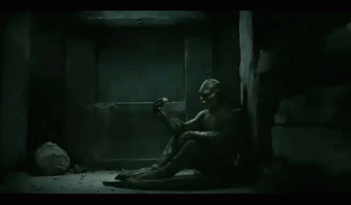 A Statue Of A Man Is Sitting On The Floor In A Dark Room . GIF