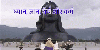 A Statue Of A Man Sitting In Front Of A Large Statue Of A Man GIF
