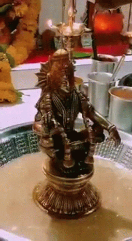 A Statue Of A Man Sitting On A Pedestal With A Bowl Of Liquid In Front Of Him GIF