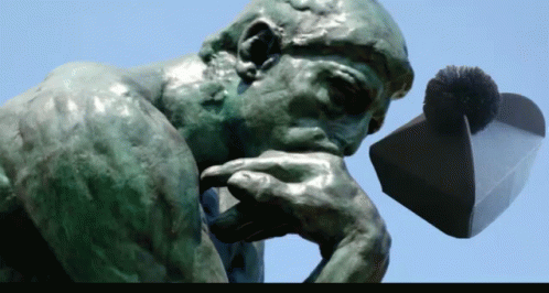 A Statue Of A Man Thinking With His Hand On His Chin And A Hat In The Background GIF