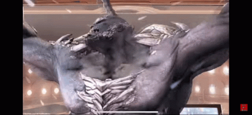 A Statue Of A Monster With Horns And Wings Is Standing In Front Of A Screen . GIF