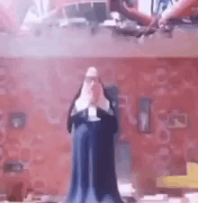A Statue Of A Nun Is Standing In Front Of A Brick Wall In A Room . GIF