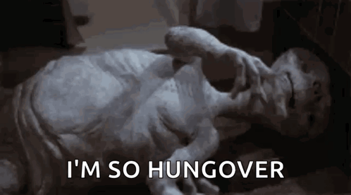 A Statue Of An Alien Is Laying On The Floor With The Words `` I 'M So Hungover '' Written On The Bottom . GIF