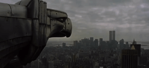 A Statue Of An Eagle Looks Out Over A City With The Twin Towers In The Background GIF