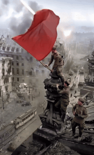 A Statue Of Soldiers Holding A Red Flag In Front Of A Destroyed City GIF