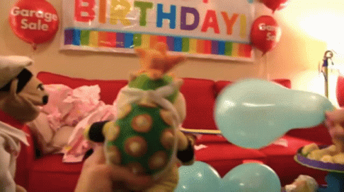 A Stuffed Animal Is Blowing Up A Blue Balloon In Front Of A Birthday Banner GIF