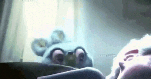 A Stuffed Animal Is Laying On A Bed Next To A Person In A Room . GIF