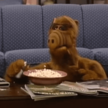 A Stuffed Animal Is Sitting At A Table With A Bowl Of Popcorn GIF