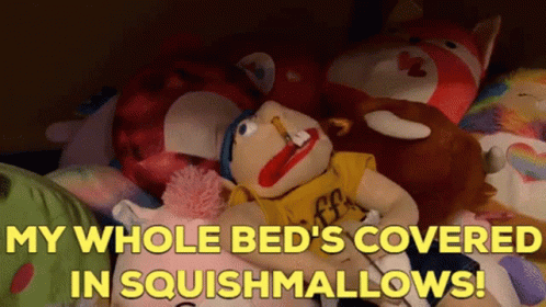 A Stuffed Animal Laying On A Bed With The Words " My Whole Bed 'S Covered In Squishmallows ! " GIF