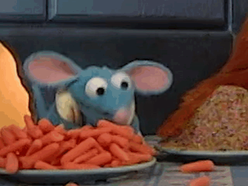 A Stuffed Animal Mouse Is Eating Carrots From A Plate On A Table . GIF