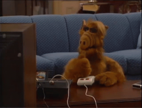 A Stuffed Animal Sitting On A Couch With A Remote Control GIF