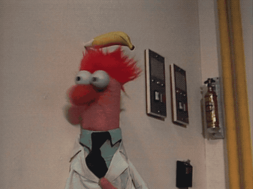 A Stuffed Animal With Bananas In Its Mouth Is Standing In Front Of A Wall With A Fire Extinguisher GIF