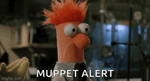 A Stuffed Animal With Red Hair And Big Eyes Is Standing In Front Of A Banana And Says `` Muppet Alert '' . GIF
