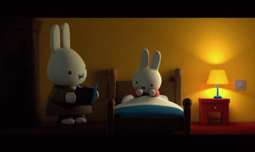 A Stuffed Bunny Is Reading A Book To Another Stuffed Bunny In Bed GIF