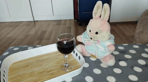 a stuffed bunny is sitting next to a glass of wine on a tray