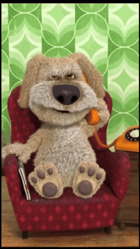 A Stuffed Dog Is Sitting In A Red Chair Talking On A Phone GIF