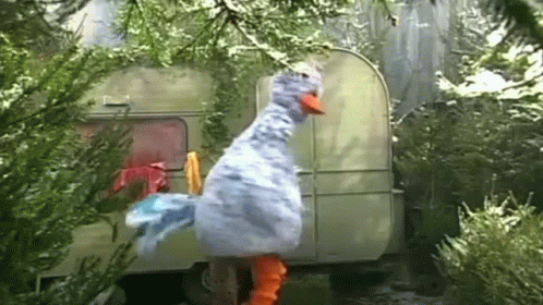 A Stuffed Duck Is Standing In Front Of A Trailer In A Forest . GIF
