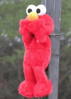 A Stuffed Elmo With A Yellow Hat Is Hanging On A Pole GIF
