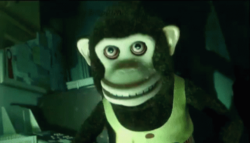 A Stuffed Monkey With Big Eyes And A Yellow Vest Is Standing In A Kitchen GIF