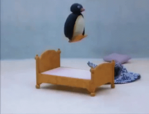 A Stuffed Penguin Is Flying Over A Small Wooden Bed GIF