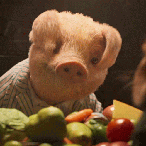 A Stuffed Pig Wearing A Striped Shirt Is Sitting In Front Of A Bowl Of Fruits And Vegetables GIF
