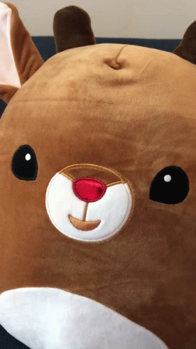A Stuffed Reindeer With A Red Nose Is Laying On A Couch GIF