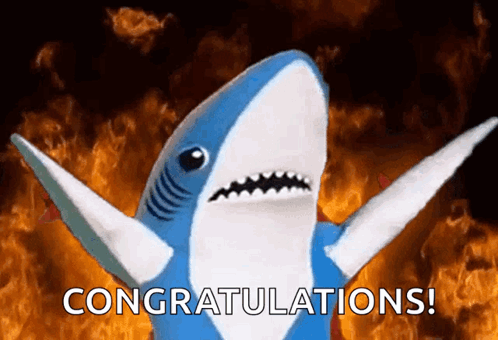 A Stuffed Shark Says Congratulations In Front Of A Fire Background GIF