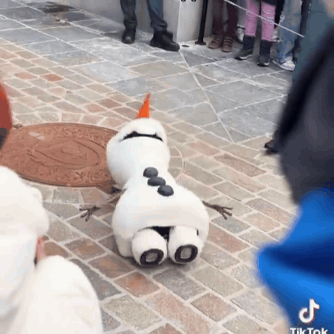A Stuffed Snowman Is Laying On The Ground With A Manhole Cover In The Background GIF