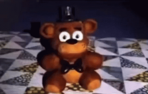 A Stuffed Teddy Bear With Big Eyes And A Bow Tie Is Sitting On A Checkered Table . GIF