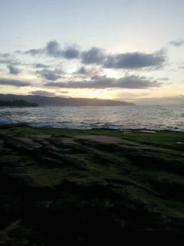 A Sunset Over A Body Of Water With A Grassy Hill In The Foreground GIF