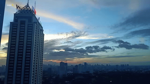 A Sunset Over A City With A Skyscraper In The Foreground That Says Shark GIF