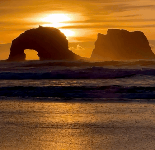 A Sunset Over The Ocean With A Large Rock Formation In The Foreground GIF