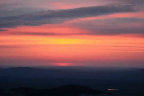 A Sunset With Mountains In The Foreground And A Dark Sky In The Background GIF