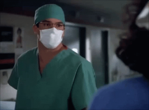 A Surgeon Wearing A Green Scrub And A Mask Talks To A Nurse GIF