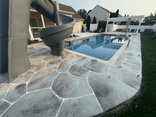 A Swimming Pool With A Slide And A Concrete Patio GIF