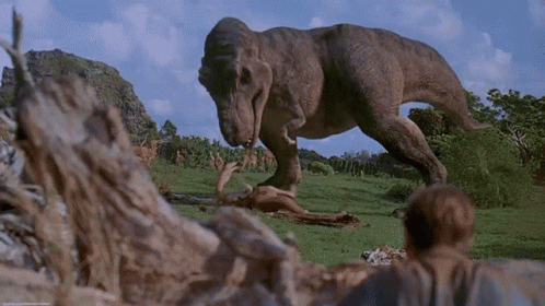 A T-Rex Is Eating A Dead Animal In The Grass GIF