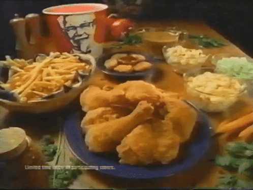 A Table Topped With Fried Chicken French Fries And Mashed Potatoes With A Kfc Cup In The Background GIF