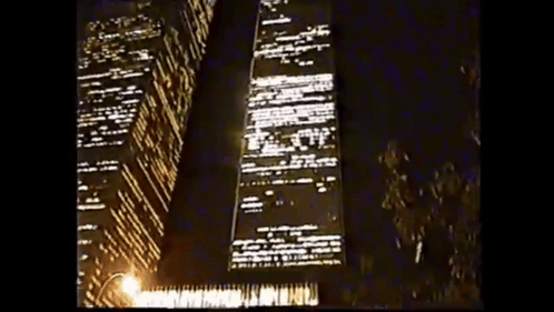 A Tall Building Is Lit Up At Night With A Street Light In The Foreground GIF