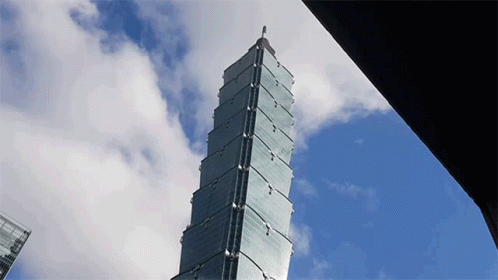 A Tall Building With A Blue Sky And Clouds In The Background GIF