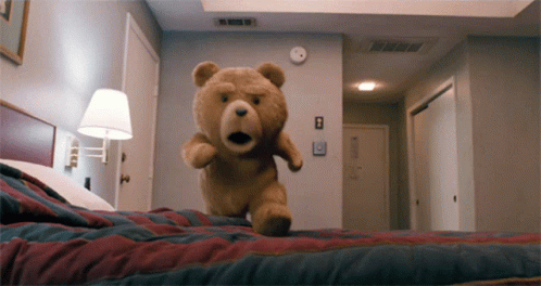 A Teddy Bear Is Jumping On A Bed In A Bedroom GIF